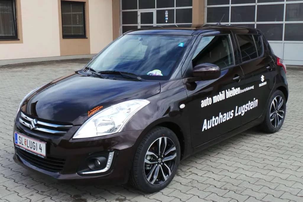 Suzuki Swift mit Beschriftung „Autohaus Lugstein“ vor der Werkstatt in Straßwalchen